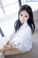 A woman sitting on a couch in a white shirt.