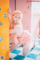 A woman in a pink and white outfit leaning against a yellow locker.