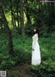 A woman in a white dress standing in the woods.