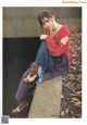 A woman sitting on a concrete ledge wearing a red shirt and blue pants.