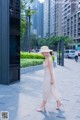 A woman in a white dress and straw hat walking down a sidewalk.