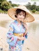 A woman in a blue kimono and a straw hat on the beach.