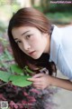 A woman in a blue and white striped shirt leaning against a bush.