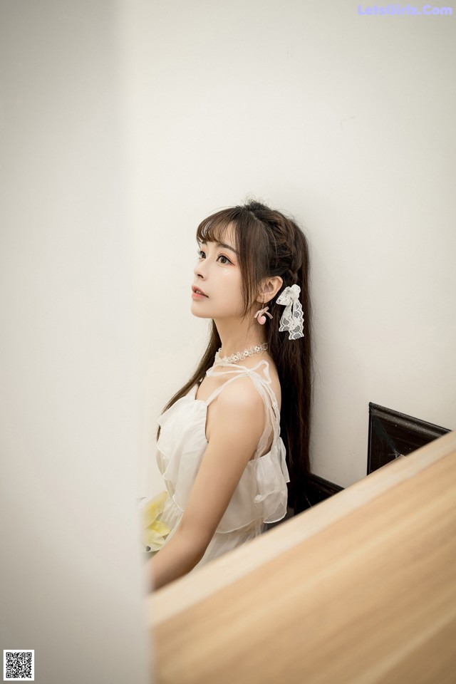 A woman in a white dress sitting on a wooden bench.